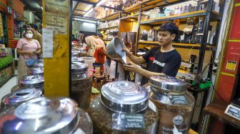 Pedagang memasukkan kopi ke dalam kemasan untuk pembeli di Dunia Kopi, Pasar Santa, Jakarta Selatan, Jumat (5/5/2023). [Suara.com/Alfian Winanto]