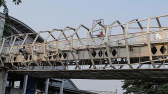 Pekerja menyelesaikan proyek pembangunan Jembatan Penyebrangan Orang (JPO) Stasiun Klender Baru di Kelnder, Jakarta Timur, Selasa (16/5/2023). [Suara.com/Alfian Winanto]