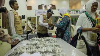 Petugas memakaikan gelang kepada jamaah calon haji embarkasi Jakarta tiba di Asrama Haji Pondok Gede, Jakarta Timur, Selasa (23/5/2023). [Suara.com/Alfian Winanto]