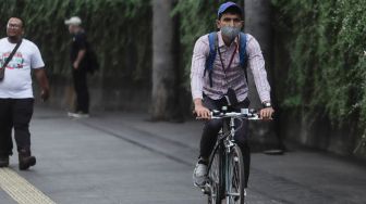 Pesepeda memakai masker saat melintas di Kawasan Bundaran HI, Jakarta, Rabu (21/6/2023). [Suara.com/Alfian Winanto]