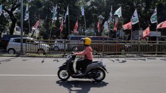 Pengendara melintas di dekat bendera parpol yang terpasang di pembatas jalan kawasan Tebet, Jakarta, Selasa (18/7/2023). [Suara.com/Alfian Winanto]