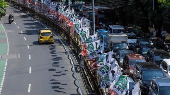 Pengendara melintas di dekat bendera parpol yang terpasang di pembatas jalan kawasan Tebet, Jakarta, Selasa (18/7/2023). [Suara.com/Alfian Winanto]