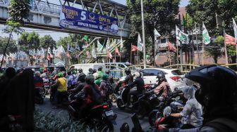 Pengendara melintas di dekat bendera parpol yang terpasang di pembatas jalan kawasan Tebet, Jakarta, Selasa (18/7/2023). [Suara.com/Alfian Winanto]