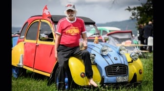 Seorang peserta berpose dengan mobil Citroen 2CV miliknya saat pertemuan Dunia ke-24 Citroen 2CV Friends di dekat Delemont, Swiss, Rabu (26/7/2023). [GABRIEL MONNET/AFP]