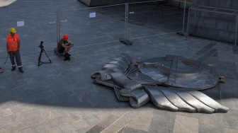 Para pekerja duduk di dekat pecahan lambang bekas Uni Soviet yang telah dibongkar dari perisai Monumen Ibu Pertiwi di Kyiv, Ukraina, Selasa (1/8/2023). [Sergii VOLSKYI/AFP]