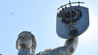 Para pekerja sedang membongkar lambang bekas Uni Soviet dari perisai Monumen Ibu Pertiwi di Kyiv, Ukraina, Selasa (1/8/2023). [Sergei SUPINSKY / AFP]