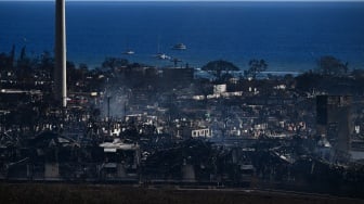 Sebuah cerobong asap berdiri di antara bangunan kota yang terbakar akibat kebakaran hutan hebat yang melanda di Lahaina, Maui barat, Hawaii, Jumat (11/8/2023). [Patrick T. Fallon / AFP]