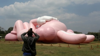 Pengunjung melihat instalasi seni dari yang dibuat oleh seniman dunia Brian Donnelly atau KAWS saat pameran bertajuk KAWS:HOLIDAY Indonesia di pelataran Candi Brahma di Kompleks Candi Prambanan, Sleman, Yogyakarta, Sabtu (19/8/2023).   [DEVI RAHMAN / AFP]