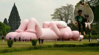 Pengunjung melihat instalasi seni dari yang dibuat oleh seniman dunia Brian Donnelly atau KAWS saat pameran bertajuk KAWS:HOLIDAY Indonesia di pelataran Candi Brahma di Kompleks Candi Prambanan, Sleman, Yogyakarta, Sabtu (19/8/2023).   [DEVI RAHMAN / AFP]