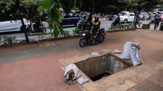 Pengendara motor menghindari lubang saluran kabel di Jalan Raya Casablanca, Jakarta, Jumat (25/8/2023). [Suara.com/Alfian Winanto]