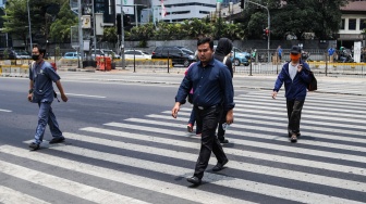 Pekerja melintasi pelican crossing di Jakarta, Senin (9/10/2023). [Suara.com/Alfian Winanto]