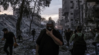 Orang-orang berjalan di atas puing-puing bangunan yang hancur akibat serangan udara Israel di Kota Gaza, Palestina, Sabtu (7/10/2023). [Mohammed ABED / AFP]