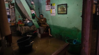 Warga beristirahat di rumahnya yang tergenang banjir di kawasan Kebon Pala, Kampung Melayu, Jakarta, Kamis (30/11/2023). [Suara.com/Alfian Winanto]