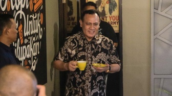 Ketua KPK nonaktif Firli Bahuri (tengah) berjalan sambil membawa kopi saat akan memulai konferensi pers di salah satu cafe di Jakarta Timur, Selasa (19/12/2023). [Suara.com/Alfian Winanto]