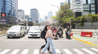 Pekerja melindungi tubuh dari terik matahari menggunakan payung saat berjalan di kawasan Sudirman, Jakarta, Kamis (21/12/2023). [Suara.com/Alfian Winanto]