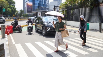 Pekerja melindungi tubuh dari terik matahari menggunakan payung saat berjalan di kawasan Sudirman, Jakarta, Kamis (21/12/2023). [Suara.com/Alfian Winanto]