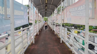 Pejalan kaki melintasi jembatan Penyeberangan Orang (JPO) yang tertutup oleh alat peraga kampanye Pemilu 2024 di Jakarta, Rabu (27/12/2023). [Suara.com/Alfian Winanto]