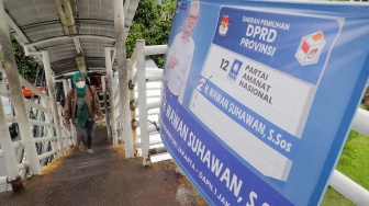 Pejalan kaki melintasi jembatan Penyeberangan Orang (JPO) yang tertutup oleh alat peraga kampanye Pemilu 2024 di Jakarta, Rabu (27/12/2023). [Suara.com/Alfian Winanto]