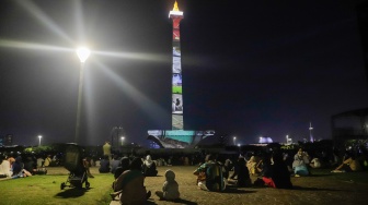 Pengunjung menyaksikan pertunjukan video mapping Monas Week di Monumen Nasional (Monas), Jakarta, Jumat (29/12/2023). [Suara.com/Alfian Winanto]