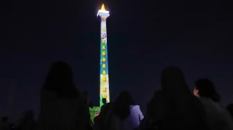 Pengunjung menyaksikan pertunjukan video mapping Monas Week di Monumen Nasional (Monas), Jakarta, Jumat (29/12/2023). [Suara.com/Alfian Winanto]