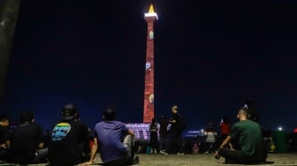 Pengunjung menyaksikan pertunjukan video mapping Monas Week di Monumen Nasional (Monas), Jakarta, Jumat (29/12/2023). [Suara.com/Alfian Winanto]