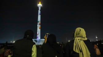 Pengunjung menyaksikan pertunjukan video mapping Monas Week di Monumen Nasional (Monas), Jakarta, Jumat (29/12/2023). [Suara.com/Alfian Winanto]