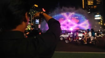 Warga menyaksikan water screen yang sedang di uji coba untuk perayaan malam tahun baru di Bundaran HI, Jakarta, Sabtu (30/12/2023). [Suara.com/Alfian Winanto]
