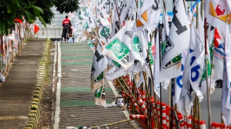 Warga melintas di samping alat peraga kampanye (APK) pemilu 2024 yang terpasang di pembatas jalur sepeda (stick cone) di kawasan Menteng, Jakarta, Selasa (9/1/2024). [Suara.com/Alfian Winanto]