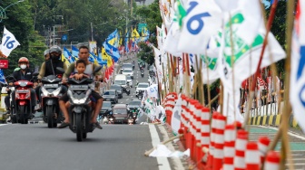 Warga melintas di samping alat peraga kampanye (APK) pemilu 2024 yang terpasang di pembatas jalur sepeda (stick cone) di kawasan Menteng, Jakarta, Selasa (9/1/2024). [Suara.com/Alfian Winanto]