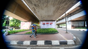 Warga melintas di samping baliho sosialisasi visi dan misi tiga pasangan calon presiden dan wakil presiden 2024 yang terpasang di kawasan Kuningan, Jakarta, Selasa (9/1/2024). [Suara.com/Alfian Winanto]