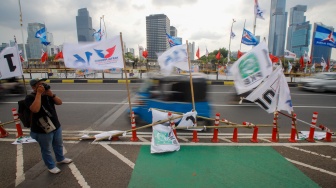 Warga melintas di samping alat peraga kampanye (APK) pemilu 2024 yang terpasang di pembatas jalur sepeda (stick cone) di kawasan Menteng, Jakarta, Selasa (9/1/2024). [Suara.com/Alfian Winanto]