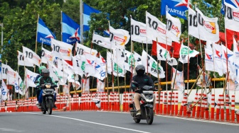 Warga melintas di samping alat peraga kampanye (APK) pemilu 2024 yang terpasang di pembatas jalur sepeda (stick cone) di kawasan Menteng, Jakarta, Selasa (9/1/2024). [Suara.com/Alfian Winanto]