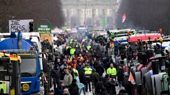 Traktor dan truk berbaris di depan gerbang Brandenburg saat berlangsungnya aksi protes para petani dan pengemudi truk di Berlin, Jerman, Senin (15/1/2024). [JOHN MACDOUGALL / AFP] 