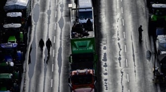 Traktor dan truk berbaris di dekat landmark gerbang Brandenburg saat berlangsungnya aksi protes para petani dan pengemudi truk di Berlin, Jerman, Senin (15/1/2024). [JOHN MACDOUGALL / AFP]