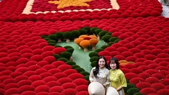 Seorang turis berswafoto di depan dupa yang disusun berbentuk bendera Vietnam di halaman desa Quang Phu Cau, Hanoi, Vietnam, Sabtu (20/1/2024). [Nhac NGUYEN / AFP] 