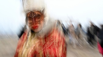 Seorang pengunjung mengenakan topeng dan kostum kuno berpose saat pra-pembukaan karnaval di Venesia, Italia, Sabtu (27/1/2024). [GABRIEL BOUYS / AFP] ​ 