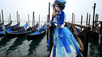 Seorang pengunjung mengenakan topeng dan kostum kuno berpose saat pra-pembukaan karnaval di Venesia, Italia, Sabtu (27/1/2024). [GABRIEL BOUYS / AFP] ​ 