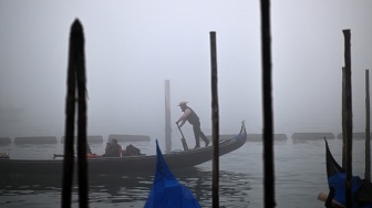 Sebuah gondola berlayar di tengah kabut saat pra-pembukaan karnaval di Venesia, Italia, Sabtu (27/1/2024). [GABRIEL BOUYS / AFP] 