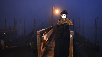 Seorang pengunjung mengenakan topeng dan kostum kuno berpose saat pra-pembukaan karnaval di Venesia, Italia, Sabtu (27/1/2024). [GABRIEL BOUYS / AFP] ​ 