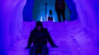 Orang-orang menikmati seluncuran es di Ice Castles di North Woodstock, New Hampshire, Amerika Serikat, Kamis (1/2/2024). [Joseph Prezioso / AFP]