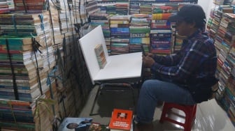 Pedagang memfoto buku dagangannya untuk dijual secara online di Sentra Buku Pasar Kenari, Jakarta, Senin (5/2/2024). [Suara.com/Alfian Winanto]