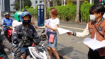 Sejumlah aktivis membagikan bunga mawar ke pengendara motor saat menggelar aksi di kawasan Bundaran Hotel Indonesia (HI), Jakarta, Selasa (13/2/2024). [Suara.com/Alfian Winanto]