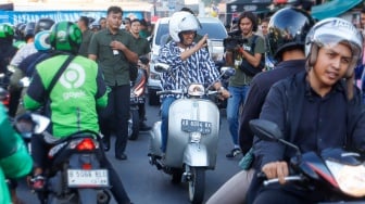 Capres nomor urut satu, Anies Baswedan menyapa warga saat mengendarai Vespa usai membeli Takjil untuk berbuka puasa di Pasar Takjil Benhil, Jakarta, Rabu (20/3/2024). [Suara.com/Alfian Winanto]