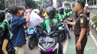 Petugas membagikan paket bantuan bahan pangan di depan Gedung Kejaksaan Agung RI, Jakarta, Senin (1/4/2024). [Suara.com/Alfian Winanto]