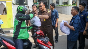 Petugas membagikan paket bantuan bahan pangan di depan Gedung Kejaksaan Agung RI, Jakarta, Senin (1/4/2024). [Suara.com/Alfian Winanto]