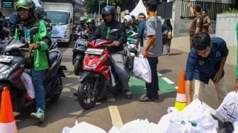 Petugas membagikan paket bantuan bahan pangan di depan Gedung Kejaksaan Agung RI, Jakarta, Senin (1/4/2024). [Suara.com/Alfian Winanto]