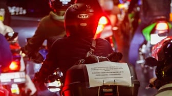 Kertas berisi pesan - pesan terpasang di belakang kendaraan pemudik bersepeda motor yang melintas di Jalan Inspeksi Kalimalang, Jakarta, Sabtu (6/4/2024). [Suara.com/Alfian Winanto]