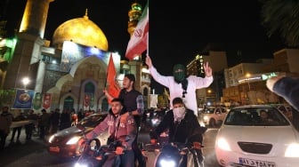 Demonstran mengibarkan bendera Iran dan bendera Palestina saat mereka berkumpul setelah Iran melancarkan serangan drone dan rudal ke Israel di Lapangan Palestina di Teheran, Iran, Minggu (14/4/2024). [ATTA KENARE / AFP]