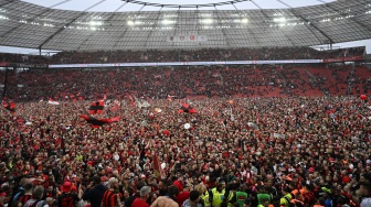 Para suporter Bayer Leverkusen berselebrasi di tengah lapangan setelah pertandingan sepak bola Bundesliga antara Bayer Leverkusen dan Werder Bremen di Leverkusen, Jerman barat, Minggu (14/4/2024). [INA FASSBENDER / AFP]