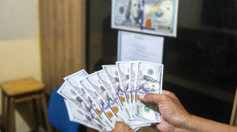 Petugas menunjukan uang dollar AS di Money Changer, Jakarta, Rabu (17/4/2024). [Suara.com/Alfian Winanto]